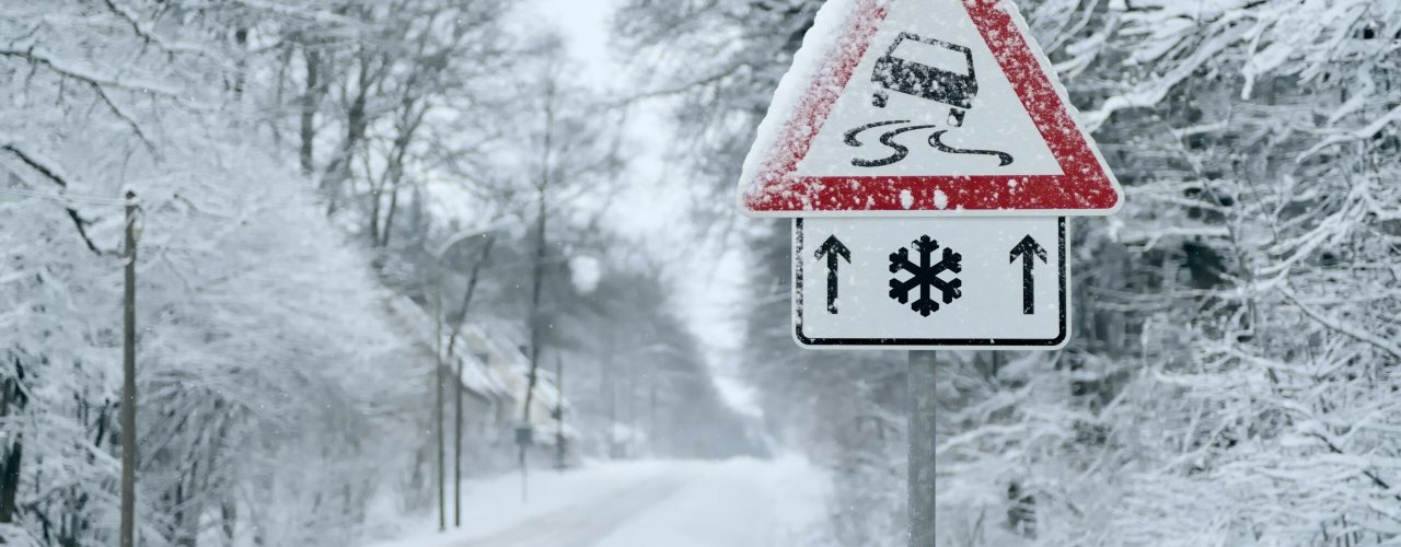 glatte verschneite Straße mit Warnschild